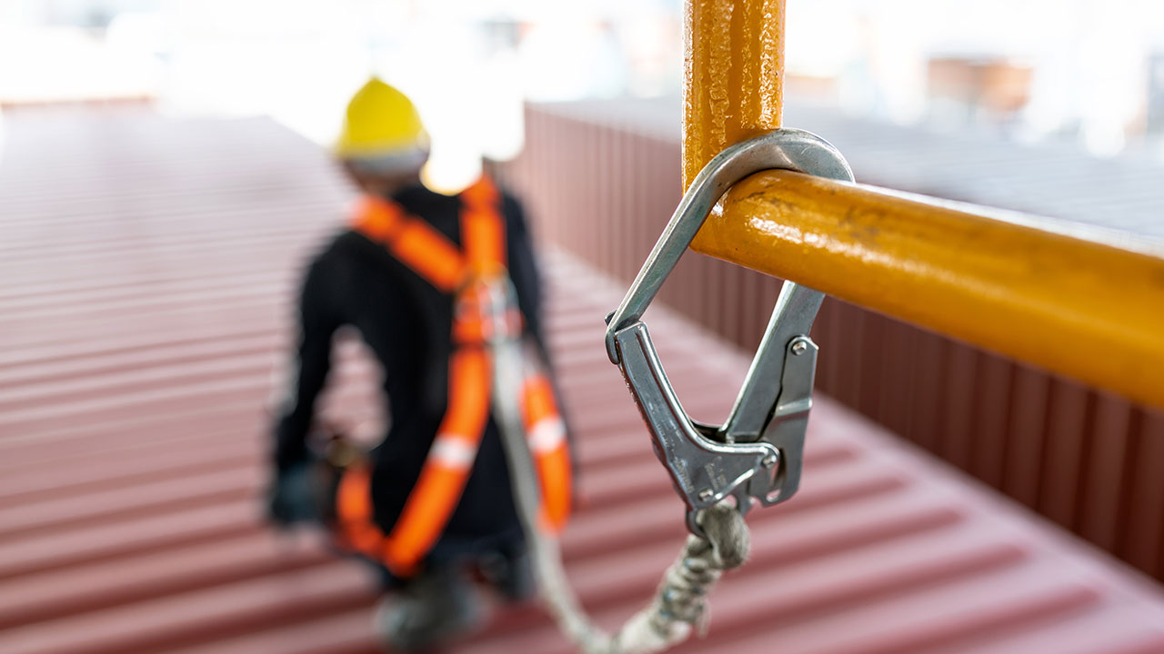 Close-up of a safety harness clip secured to railing with worker in background