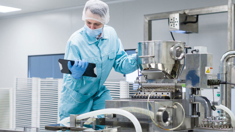 Worker in cleanroom protective clothing using a tablet beside industrial equipment