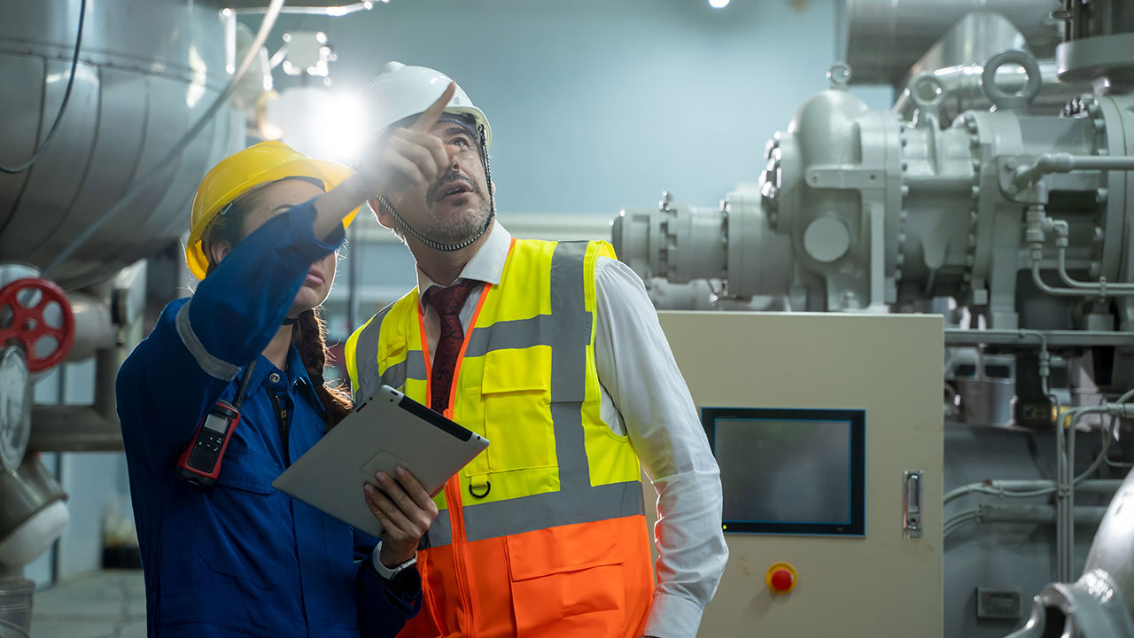 Engineers wearing safety helmets and vests inspect industrial equipment in a factory