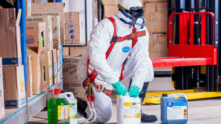 Worker in protective suit handling hazardous chemical containers in a warehouse