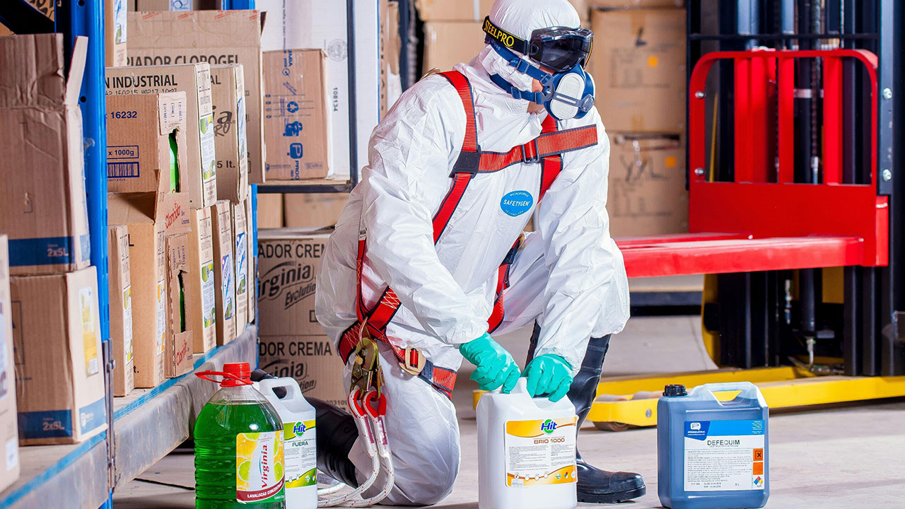 Worker in protective suit handling hazardous chemical containers in a warehouse