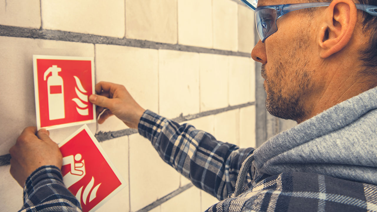 Worker wearing goggles placing fire safety signs on a wall