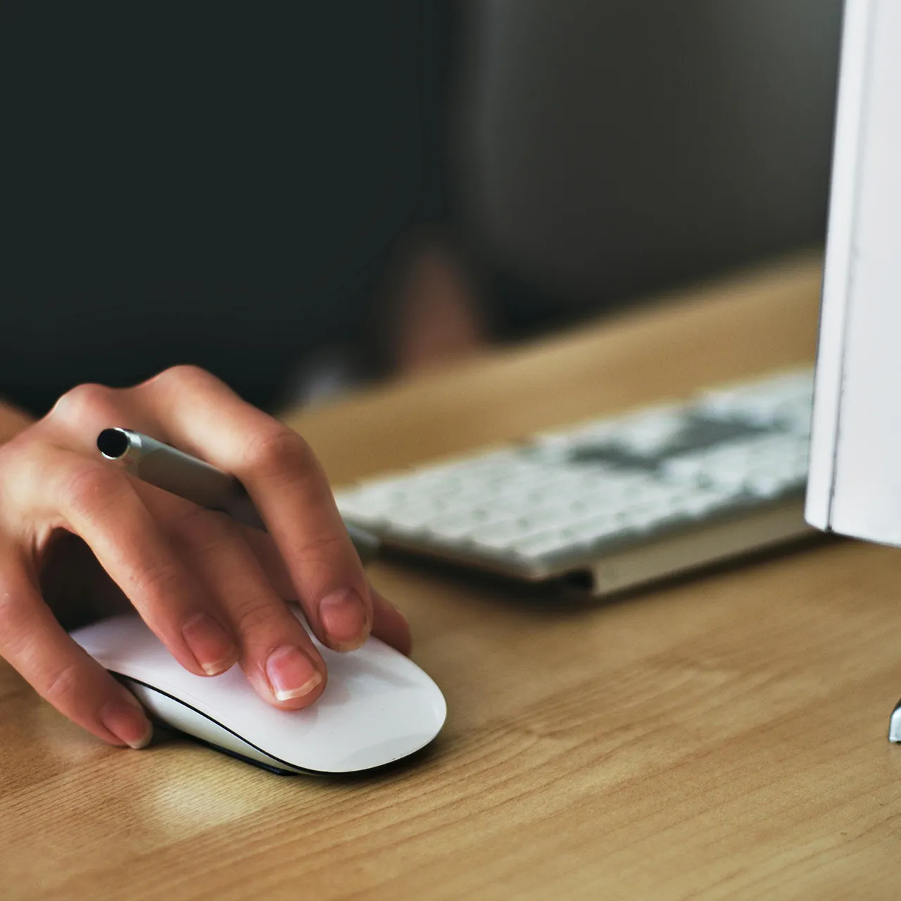 Close-up of a hand using a computer mouse next to a keyboard on a desk