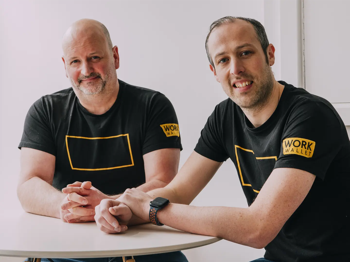 Two Work Wallet team members sitting at a table smiling at the camera