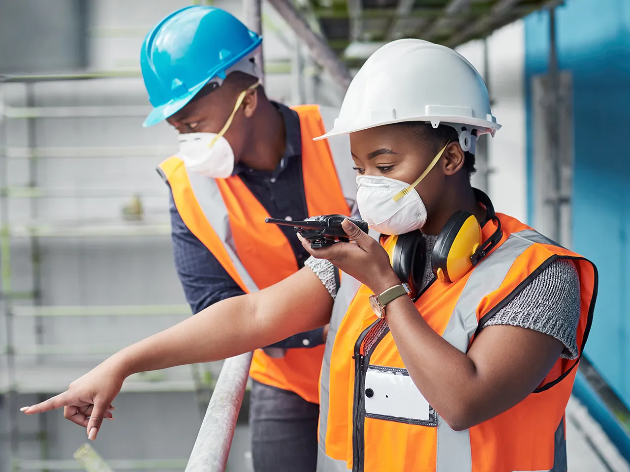 Two construction workers wearing masks and safety gear inspecting site