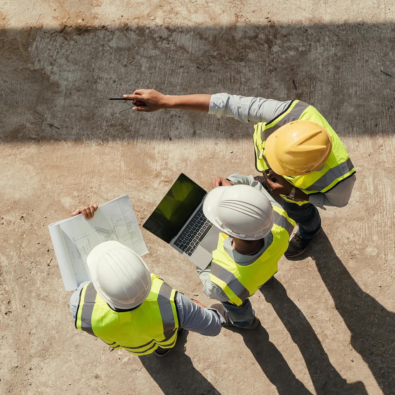 Three construction workers review plans and a laptop while discussing a site layout