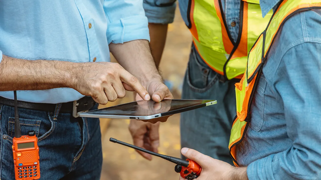 Three workers on site reviewing information together on a tablet device