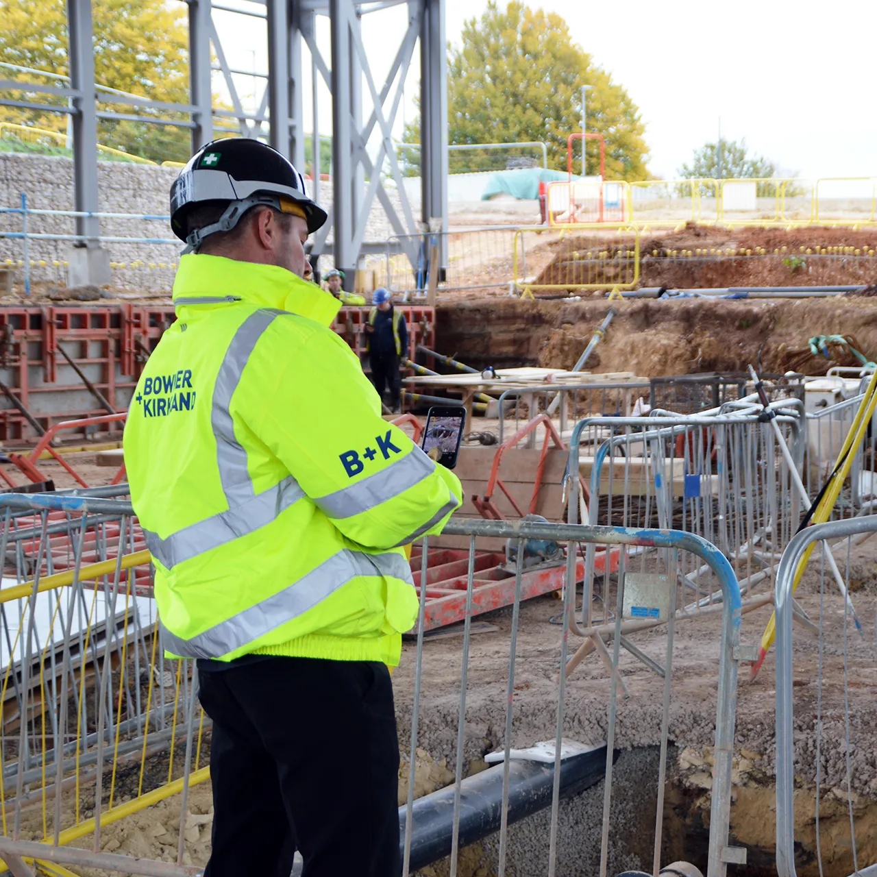 Construction manager in B+K jacket inspecting a site with a tablet