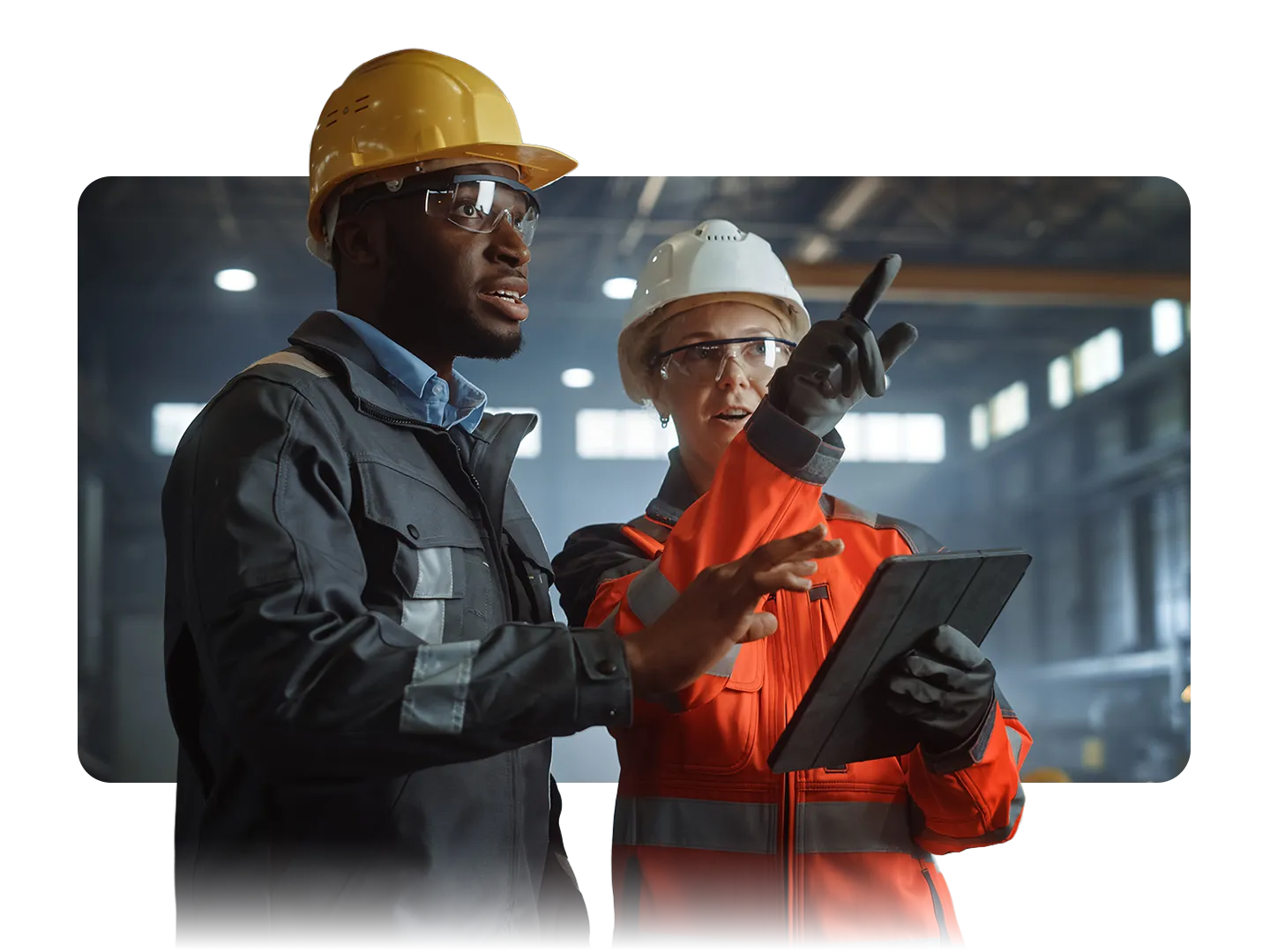 Two engineers in safety gear reviewing plans on a tablet inside an industrial building