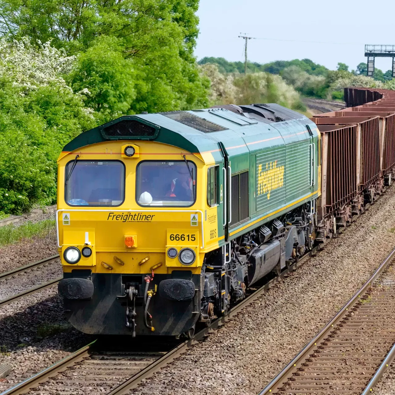 A green and yellow Freightliner cargo train travels along railway tracks