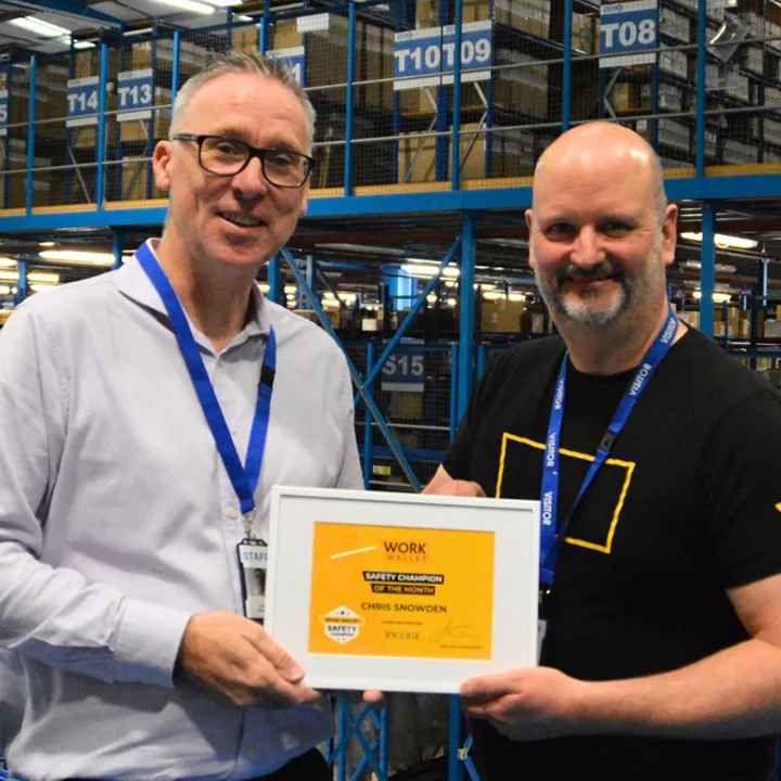 Two people standing in a warehouse holding a Safety Champion certificate