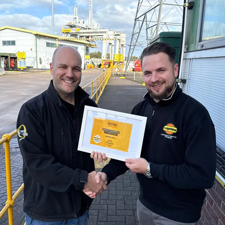Two workers shaking hands outside, one holding a Safety Champion certificate