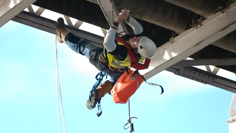 Worker suspended on ropes performing maintenance under a metal structure
