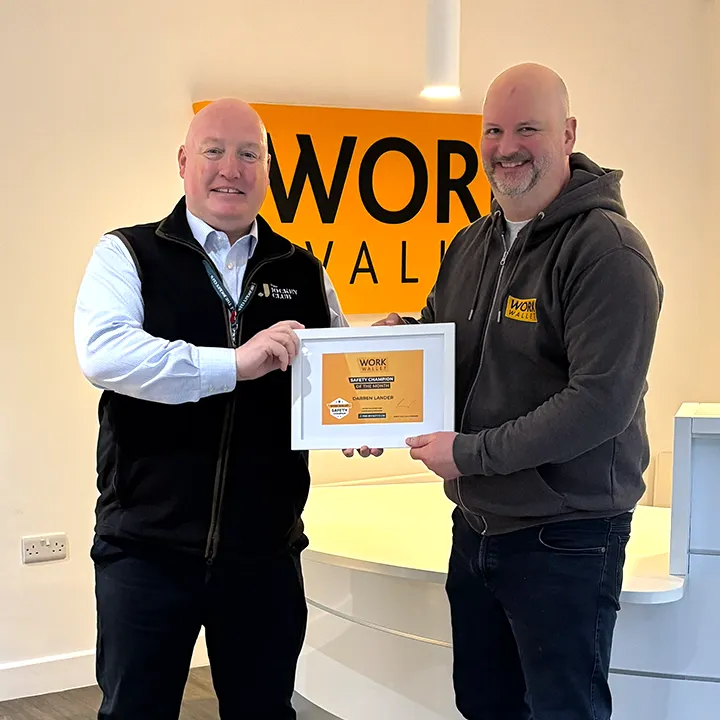 Two men smiling as one hands the other a framed Work Wallet Safety Champion award