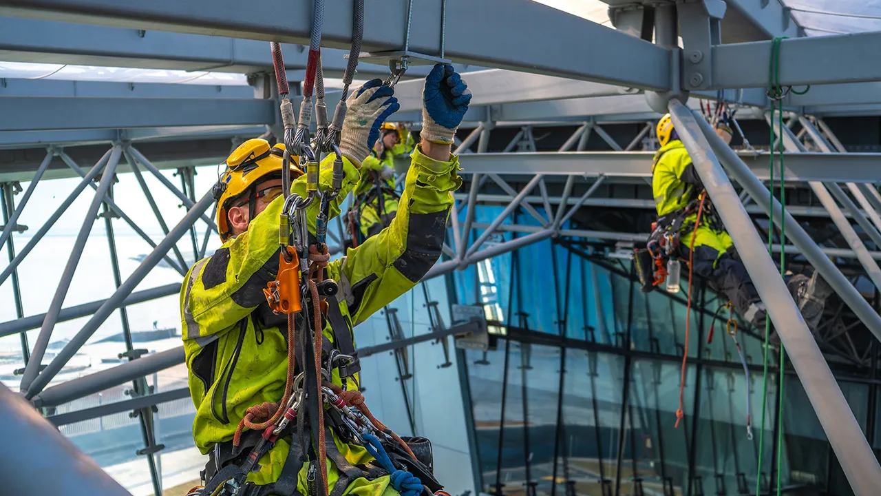 Workers in safety gear use ropes and harnesses while inspecting a steel structure