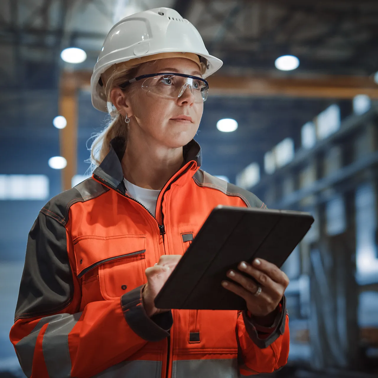 Worker in safety gear using a tablet inside an industrial facility