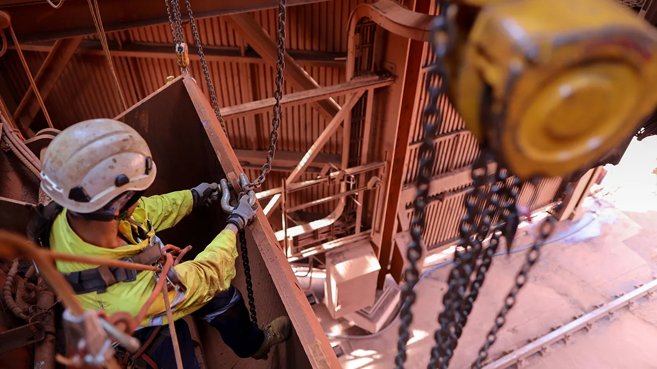 Worker in safety harness and helmet attaching chains while working at height inside an industrial site