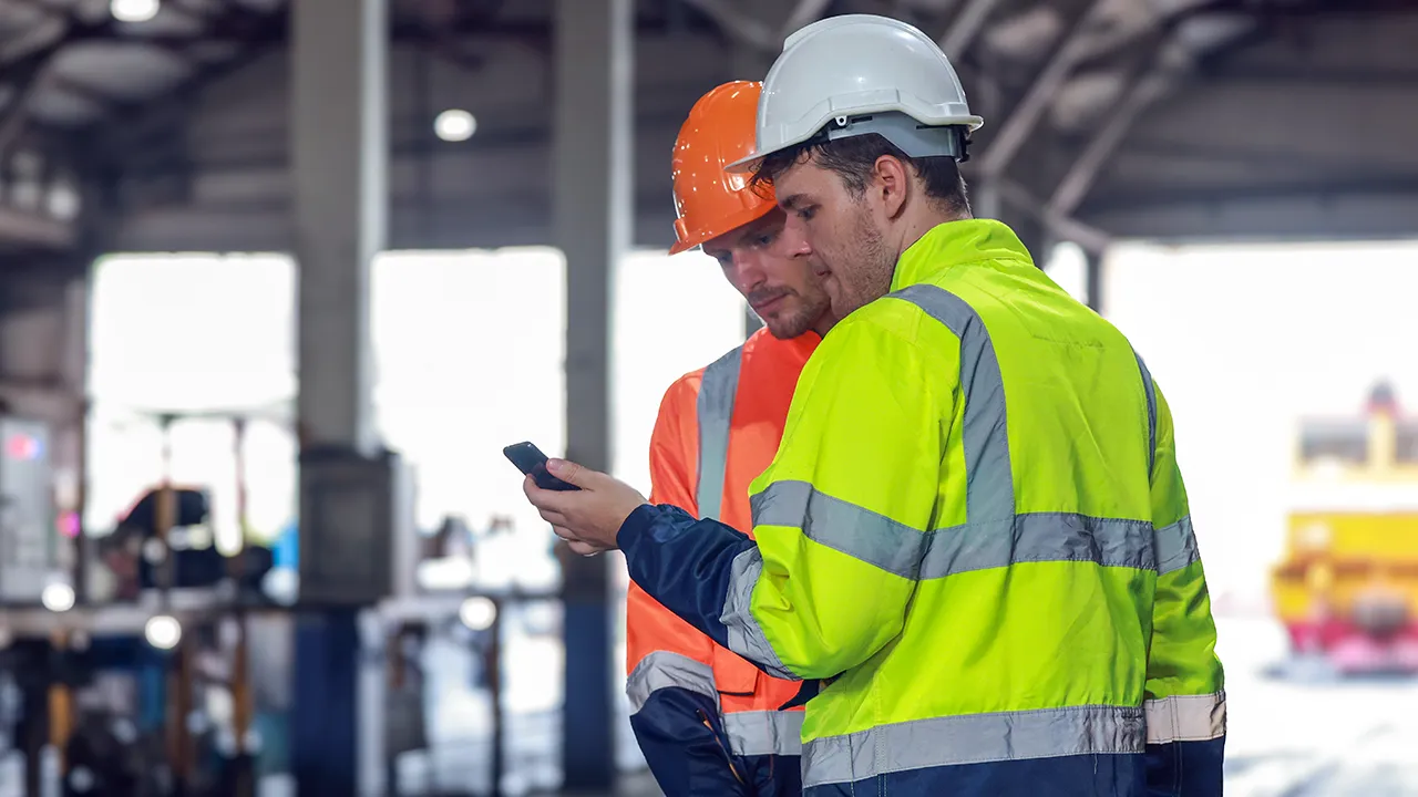 Two workers in hard hats and high-visibility jackets reviewing a phone at a job site