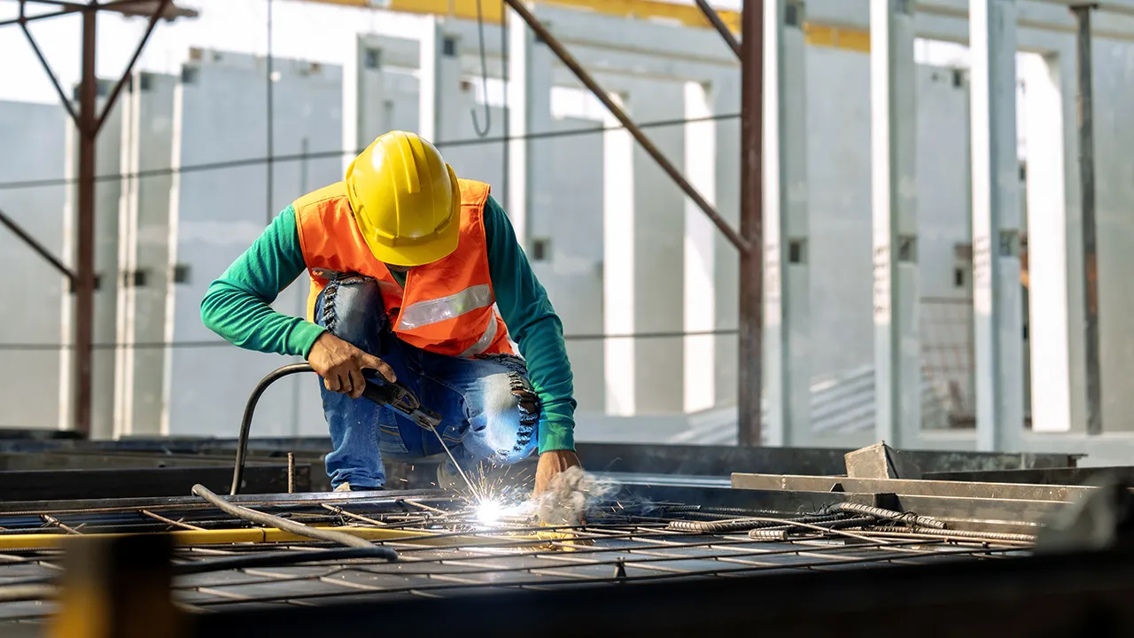 Construction worker welding rebar grid on building site wearing hard hat and safety vest